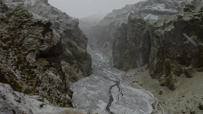 The snow is falling on the stream between the mountains