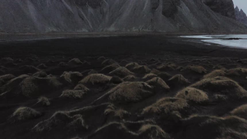 A vehicle slowly traveling along a road on a rocky coast at the base of a mountain ridge