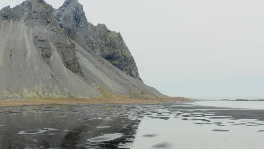 A mountain is reflected in sandy puddles on an overcast day