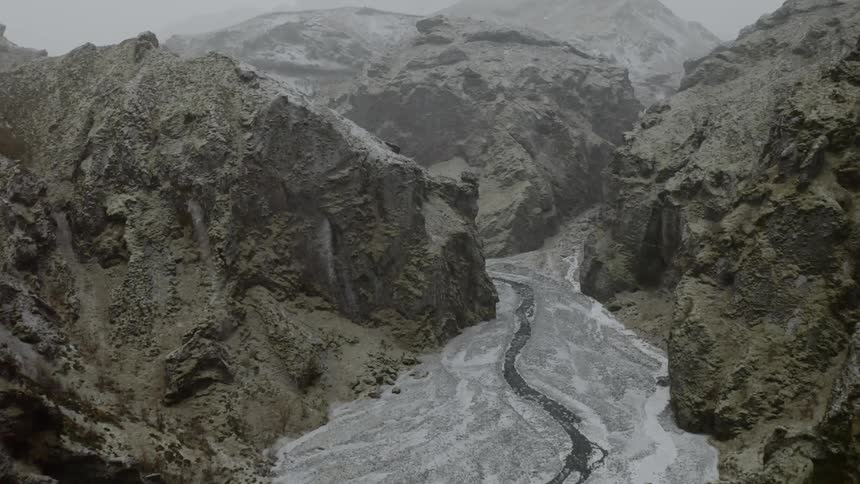 A stream flows through the rocky surface of a mountain as it snows