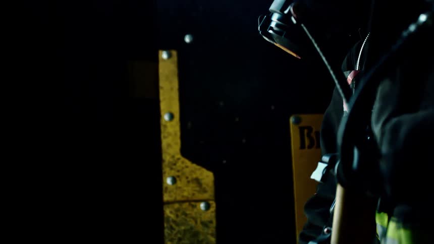 A firefighter wearing a face mask and respirator closes a large door which shuts out all the smoke and the light