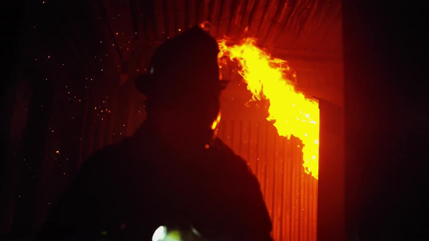 A firefighter walks away from the flames carrying a flash light