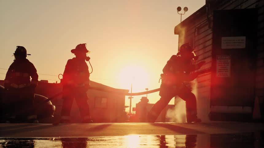 Firefighters holding a hose rush towards a building