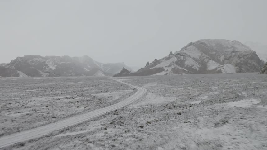 A snow covered roadway surrounded by flat land and hills in the distance