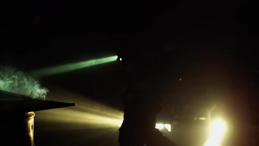 A firefighter with a flashlight walks the site of a recently extinguished fire with smoke still rising and water dripping down