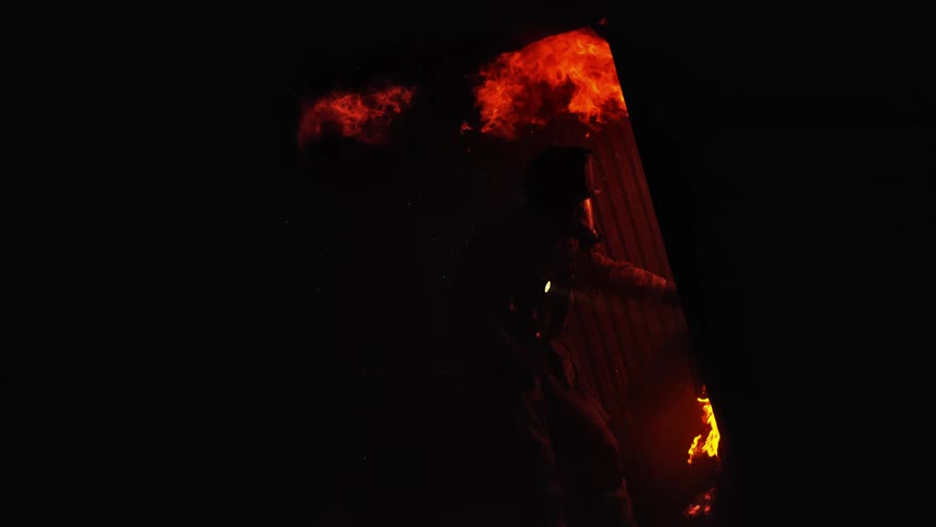 Fireman accessing fire from doorway of burning building at night