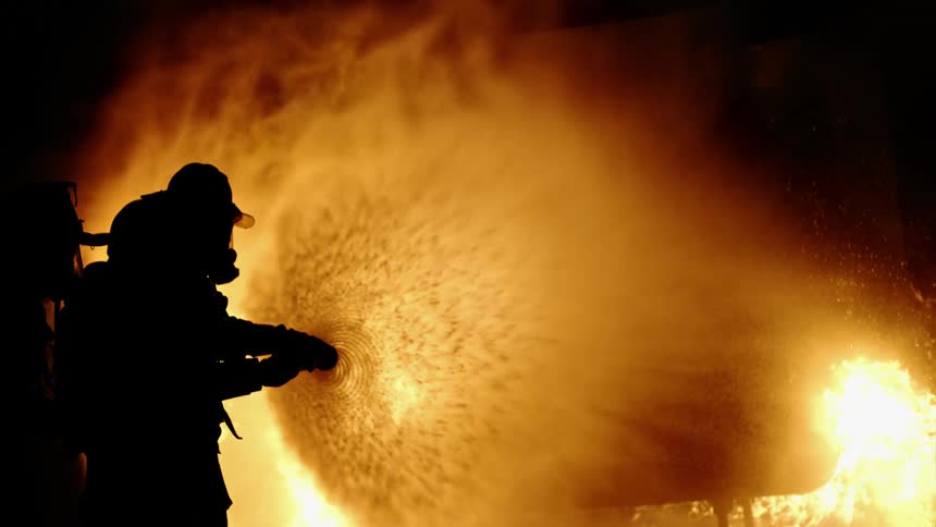 A firefighter uses a hose on a roaring fire at night