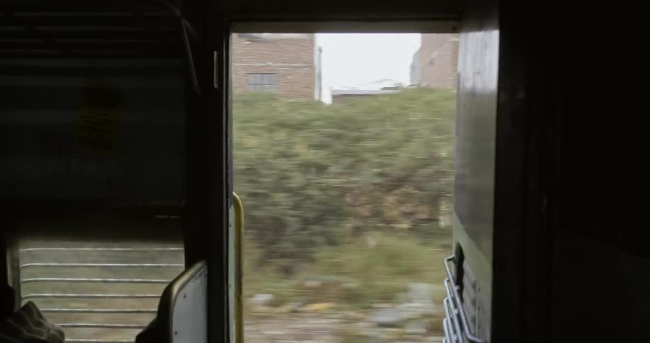 Buildings and trees pass by open door of train