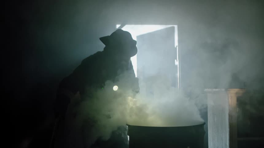 Firefighter in full gear inspecting smoking barrel inside shack