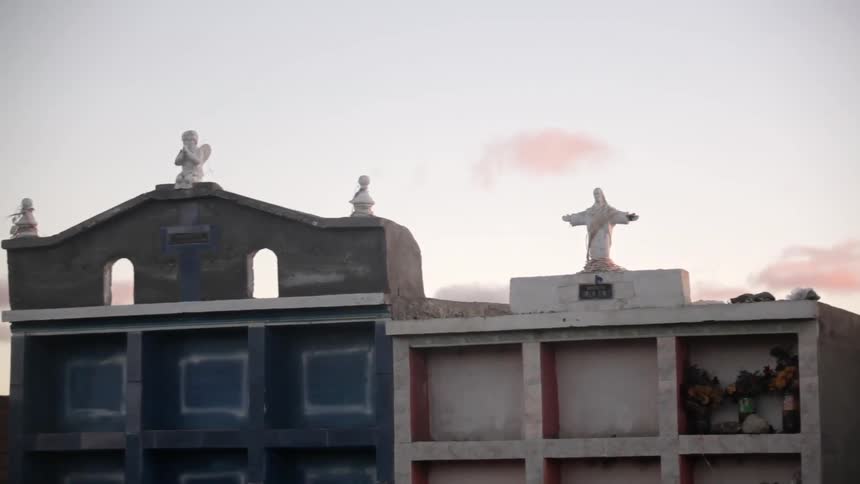 The sun rises behind a crypt with a statue of Jesus on it
