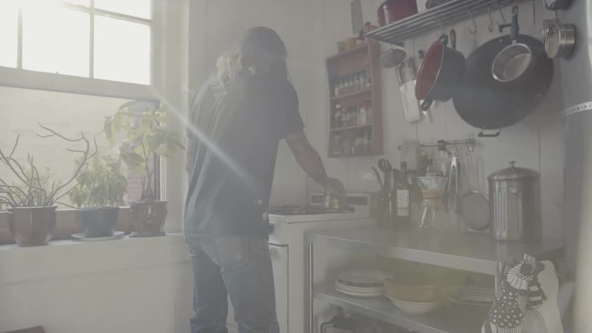 Long haired man boils water in pot on the stove in the kitchen