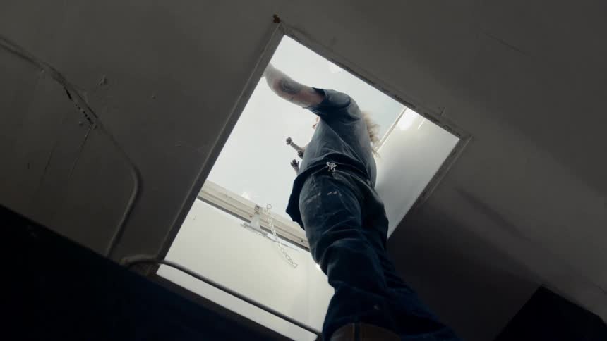 A worker stands in the opening of a ceiling access door while holding a cat