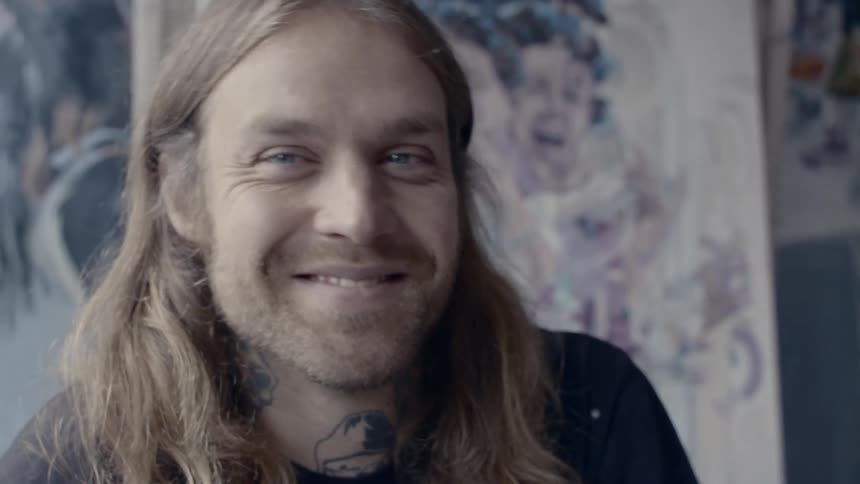 Long haired blonde man sitting before the wall chuckles