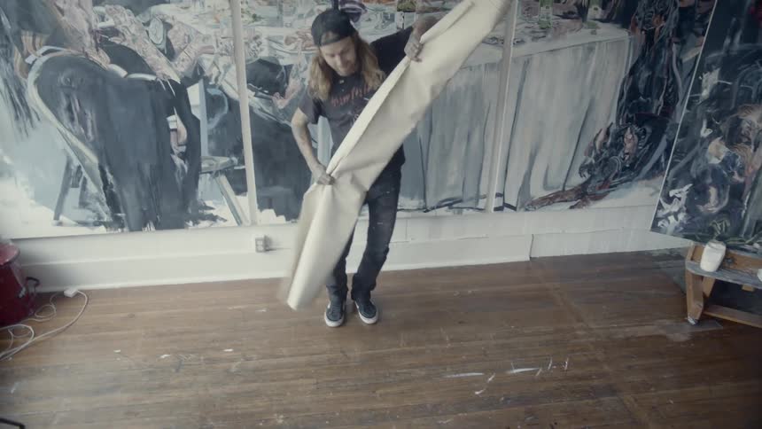 A male artist in an art studio unrolls a large canvas onto the floor