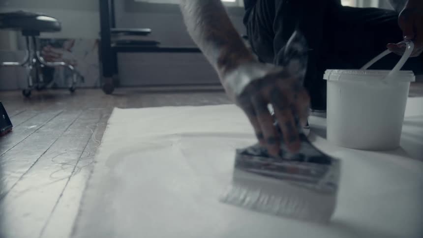 A man paints a tapestry on the floor with white paint