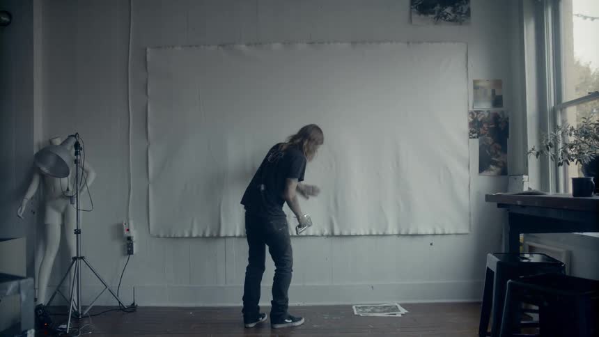 A man staples a large white canvas to a wall near a large window