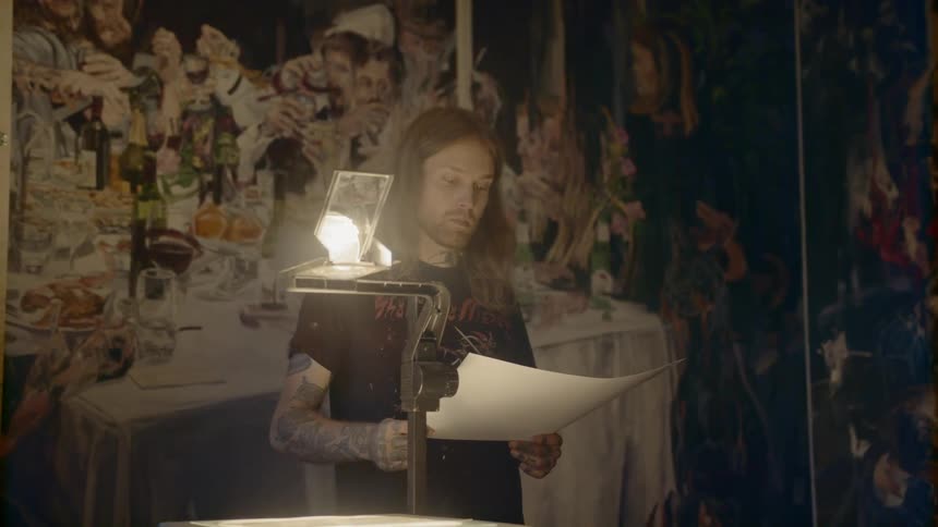 The light from an overhead projector glares while a man stands holding paper and examining artwork on the walls