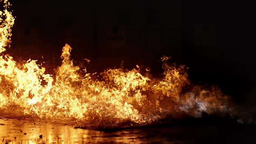 A raging fire burns and spreads across the ground in a darkened area