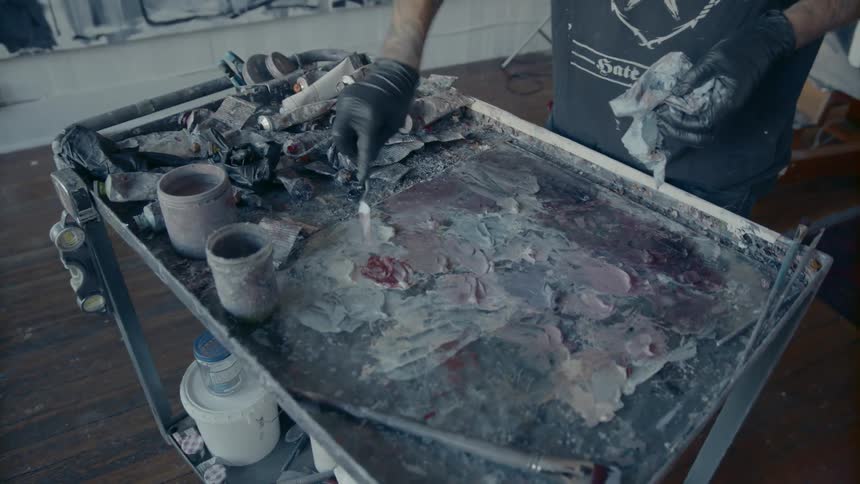 A man brushes different paint and mediums together on a large cart