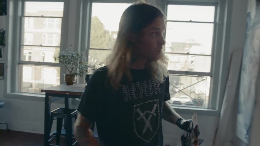 Long haired male painter paints a large canvas in the workshop