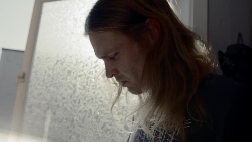 Man looks at a book as he stands near an open window