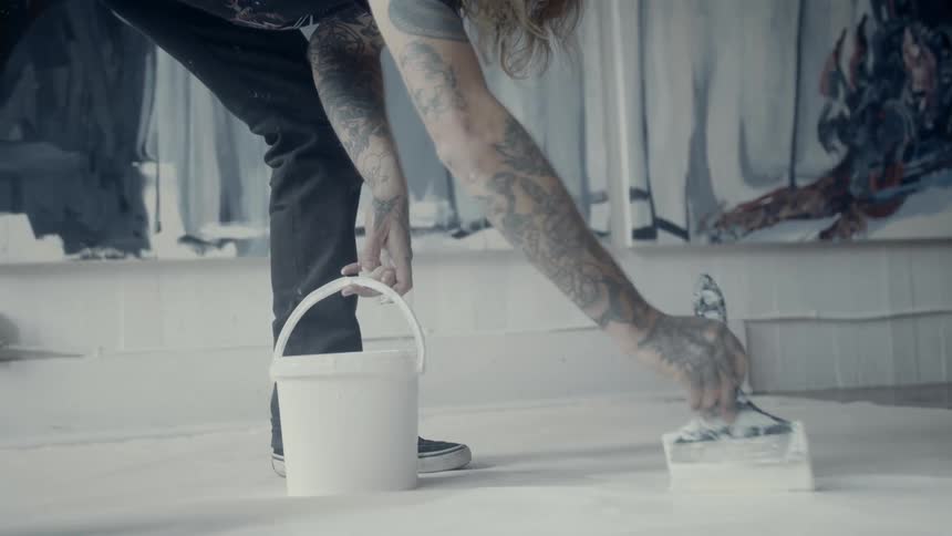 Man paints floor with white paint next to wall mural