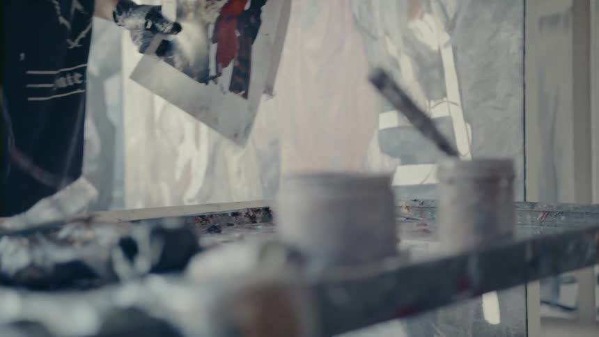 A man with black gloves cleaning paint off a paint brush