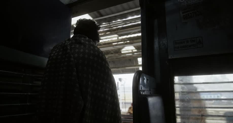 A man sits on a train and looks out into an india train station