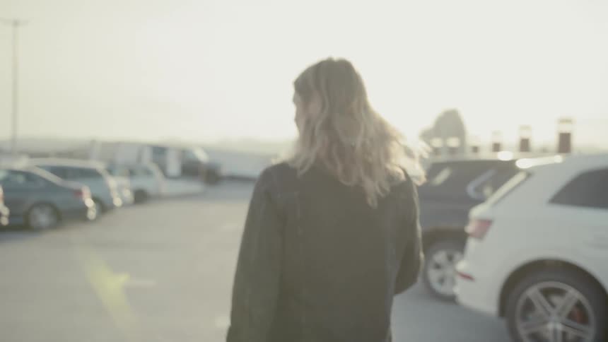 Long haired blonde man gets out of the building and walks in the parking lot