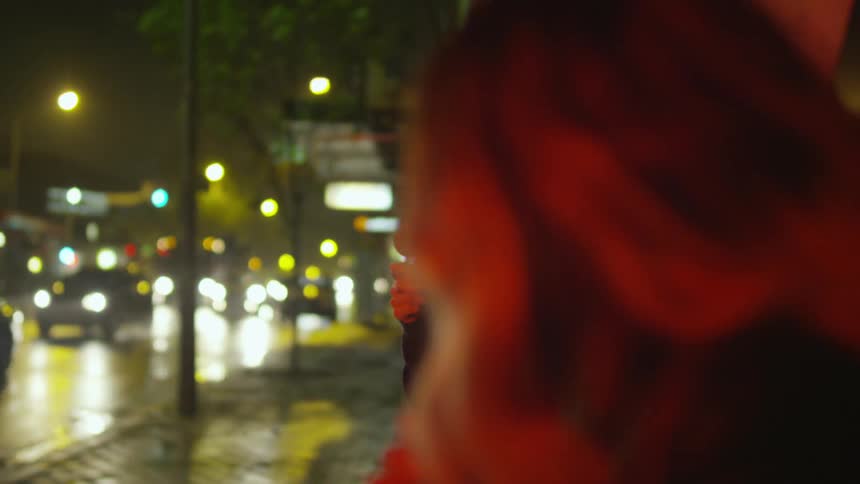 A man and a woman standing on a city street at night while they eat ice cream bars, talk and laugh