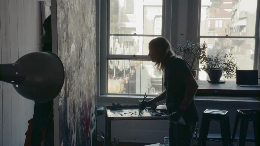 Long haired male painter paints a large canvas in the workshop