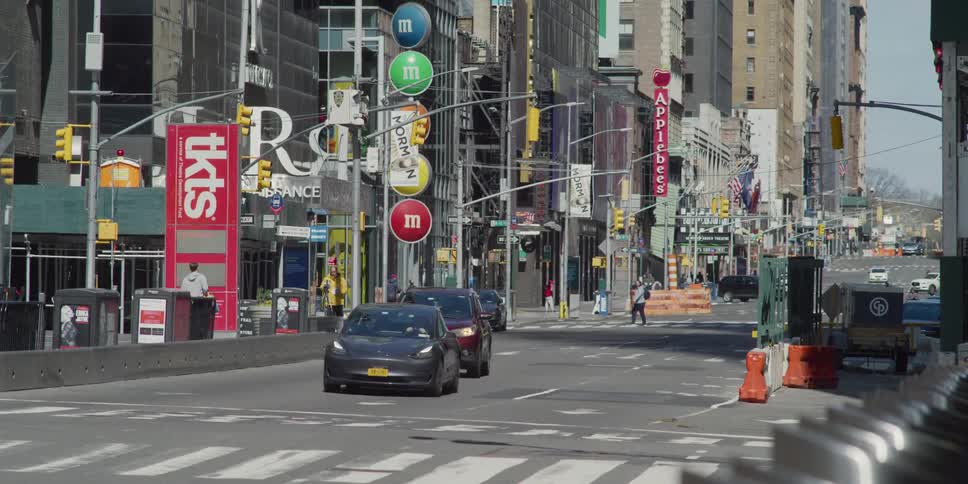 Two automobiles drive along a city street lined with numerous buildings