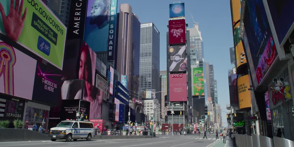 Pedestrians cross the city street as advertising signs sit on the buildings