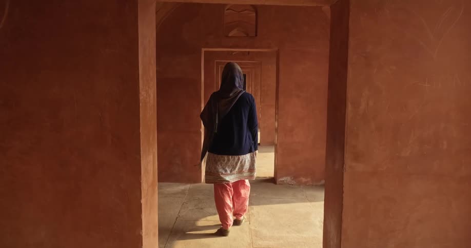 A hooded woman walks through red arches
