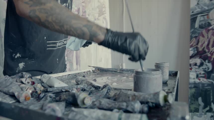 Long haired male painter paints a large canvas in the workshop