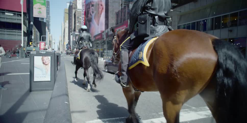 Two mounted police officers ride horses down a city street