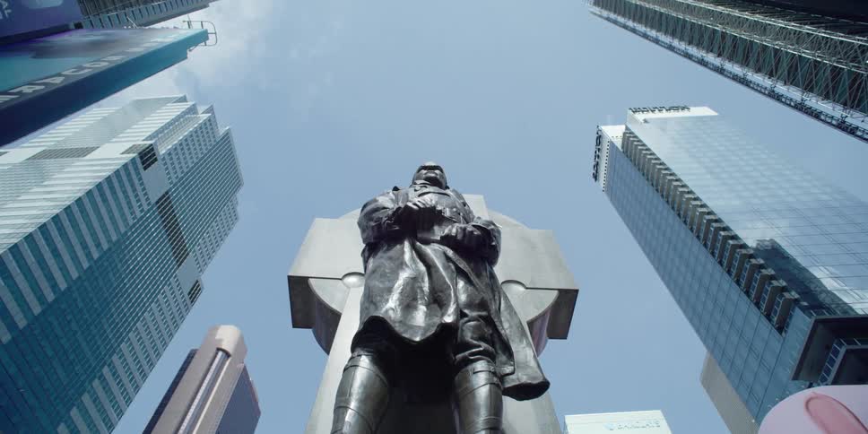 A statue of a man sits in the middle of tall skyscrapers