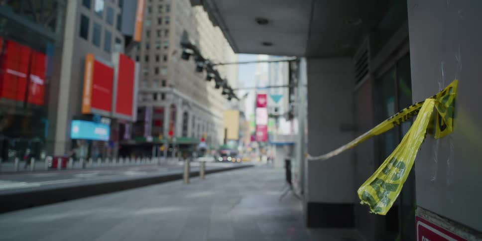 Caution tape taped to a city building flutters in a breeze as cars drive by on the city street