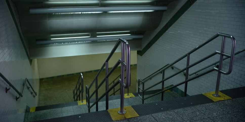 A dimly lit stairway with multiple handrails leads to a large corridor
