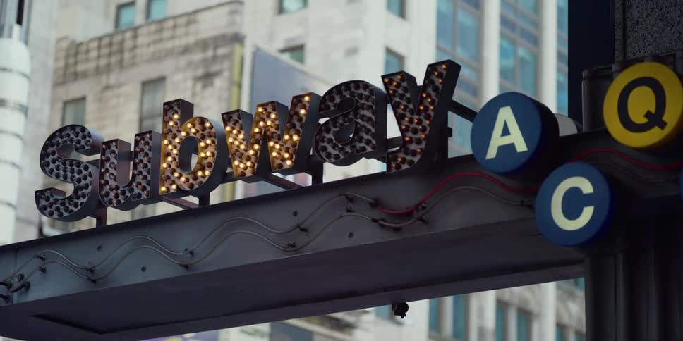Subway sign blinks near skyscraper