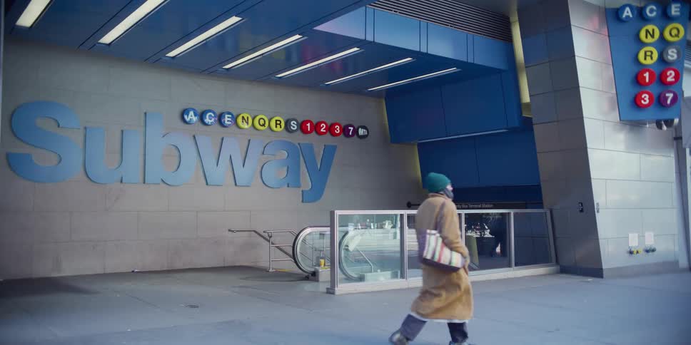 Woman in long coat walks in front of subway entrance