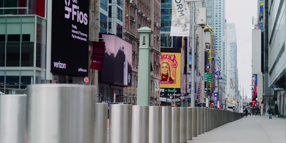 Pedestrians walk along a sidewalk in a downtown metropolitan area lined with skyscrapers