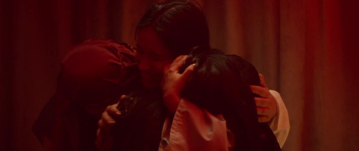 A group of actors in costume embrace each other while onstage