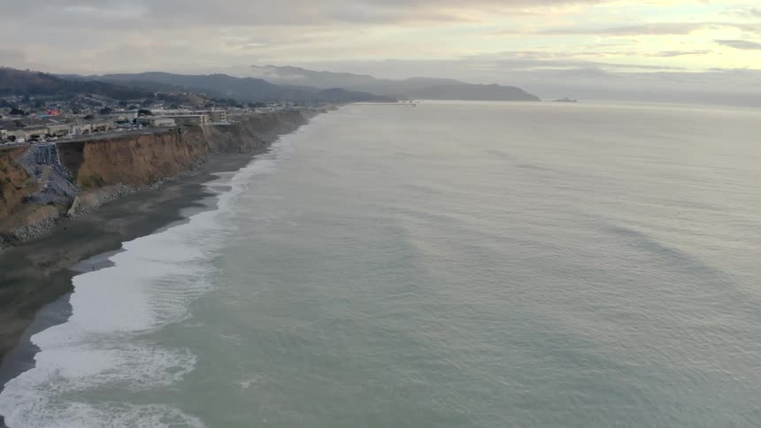An aerial view of ocean waves flowing towards a sandy beach at sunset