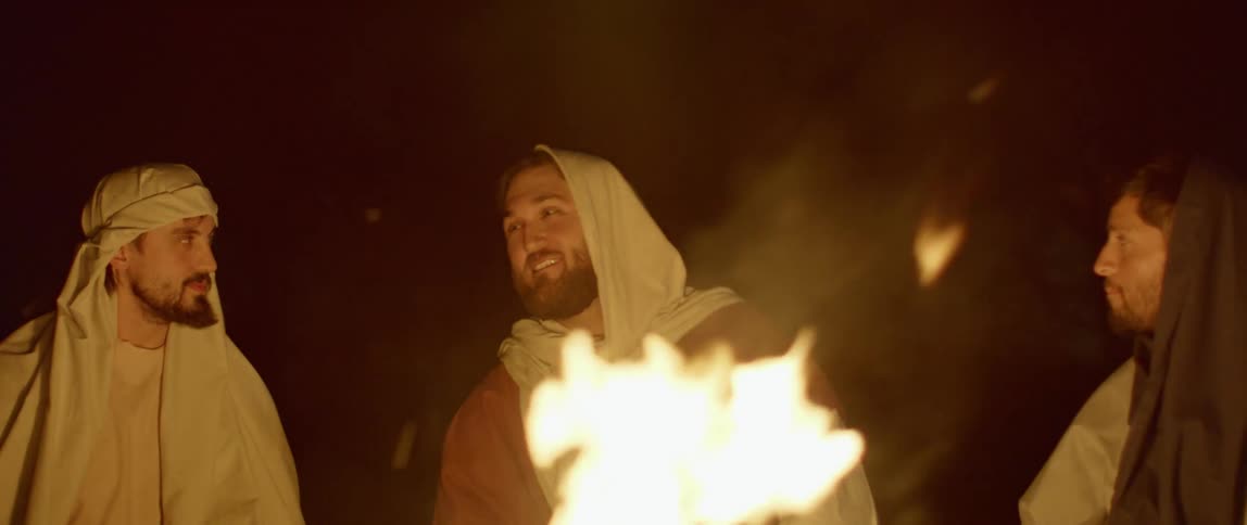 Men wearing robes and head scarves sit around a fire at night