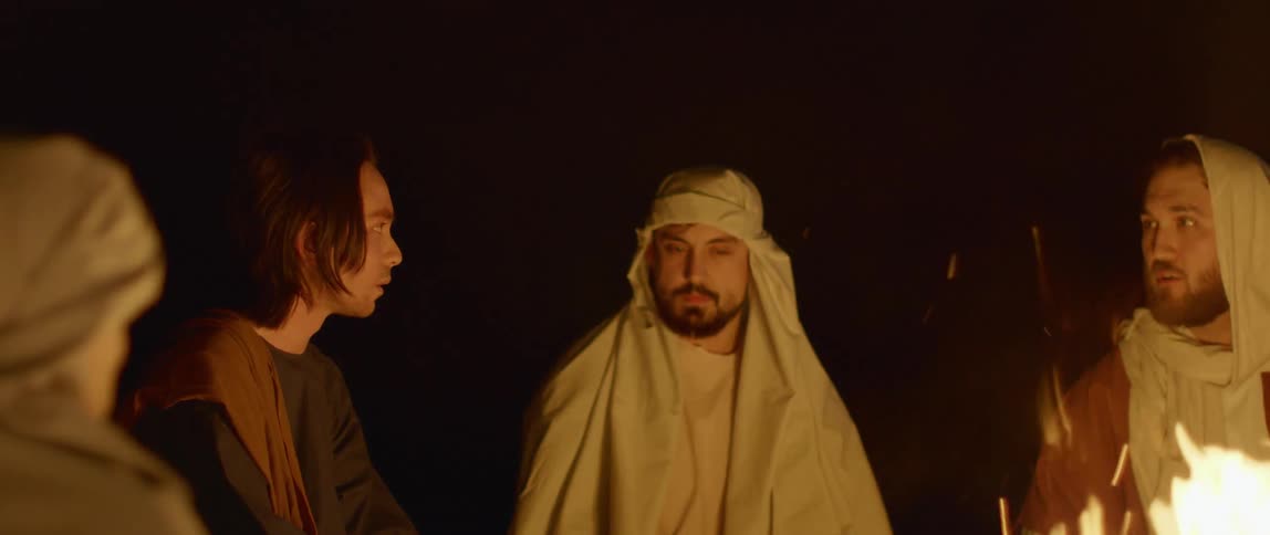 Men in biblical era robes talk around a campfire