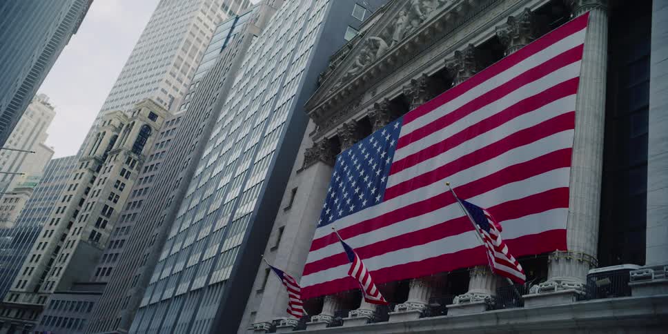 Three american flags wave in the wind in front of a giant flag across the columns of the new york stock exchange building