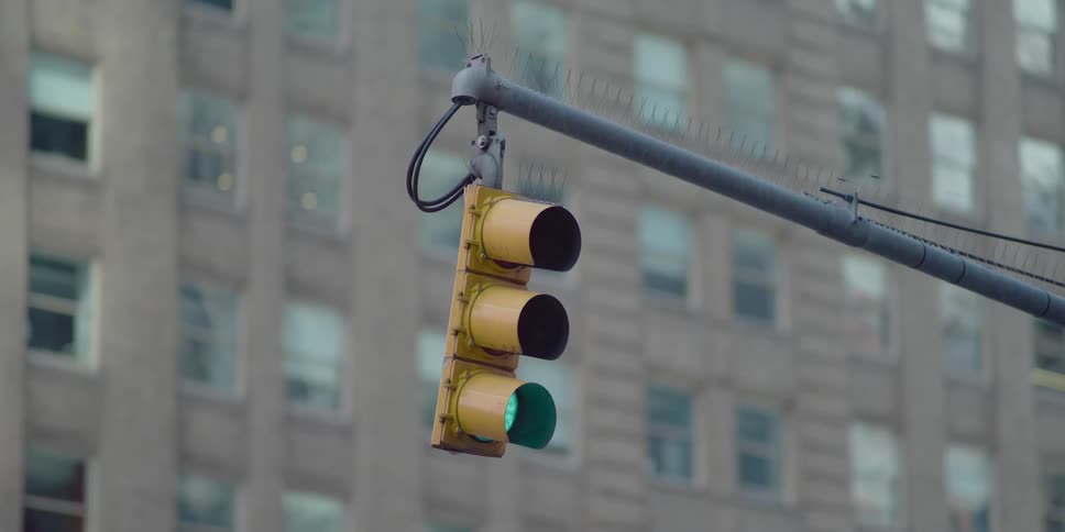 Close up a yellow traffic light hanging from a pole in a small town