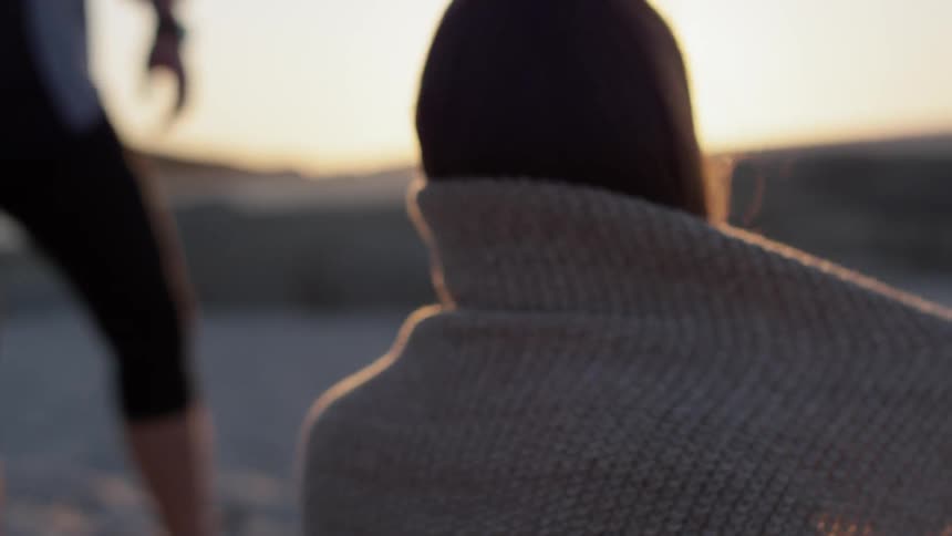 A woman wraps a blanket around her shoulders on a sunny beach
