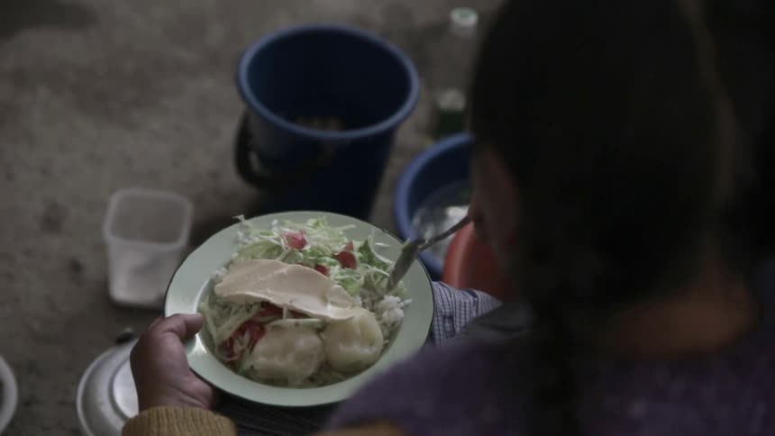 An over-the-shoulder view of a woman that's seated and eating from a plate of food